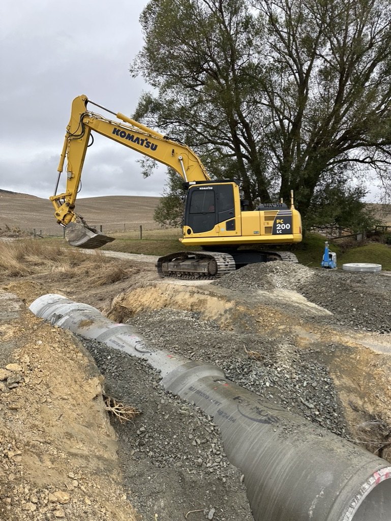 Shaw Civil Komatsu PC200 excavator laying a large concrete culvert pipe